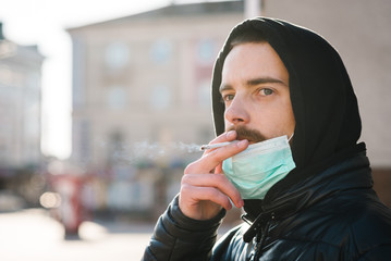 Smoking. Closeup man with mask during COVID-19 pandemic smoking a cigarette at the street. Smoking...