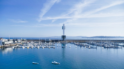Sailboats docking at port and lighthouse gainst clear summer sky.