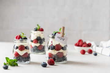 Fototapeta na wymiar Berry yogurt with fresh strawberries and blueberries in jars. Healthy breakfast parfait in glass jars. Copy space for text. Summer dessert