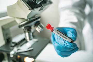 doctor wearing protective gloves holding COVID-19 blood sample test tube negative positive, using microscope researching corona virus microscopic cells testing vaccination cure, in medical laboratory