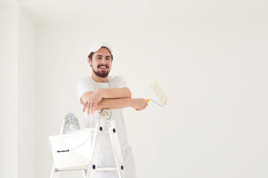 A male painter in a white uniform with a roller works in his hand in a white room