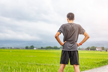 Fototapeta premium asian teen stretching his body and running along the road, exercising or practicing for a marathon race, wearing shirt, short and trainers with mountain nature and cloudy sunset sky in the background