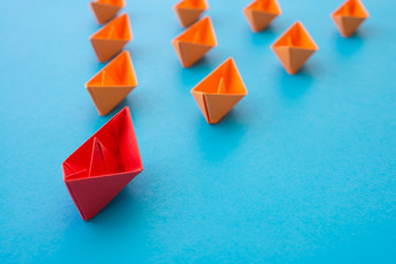 Leadership concept. Red paper boat origami motivate meeting with small orange boat on blue...
