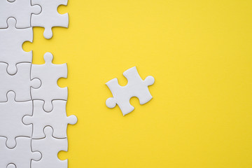 Unfinished white jigsaw puzzle on yellow background copy space. Business strategy teamwork and...