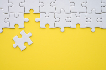 Unfinished white jigsaw puzzle on yellow background copy space. Business strategy teamwork and problem solving concept. Teamwork is collaborative effort of team to achieve goal or to complete task.