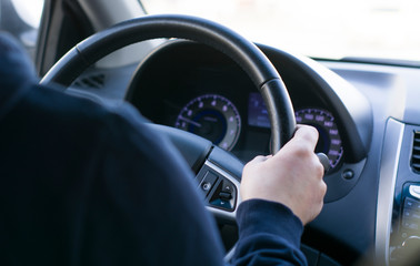 a young man is sitting at the wheel of a car, hand on the steering wheel. rear view of the dashboard