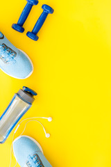Sport set with dumbbells and sneakers on yellow background top-down copy space
