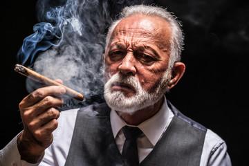 Portrait of serious senior man who is smoking cigar.