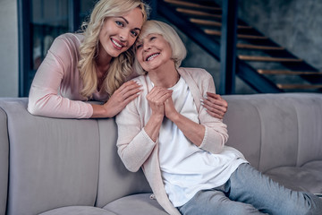 Senior woman and her attractive daughter spending time together at home and sitting on sofa. Happy Mothers' Day.