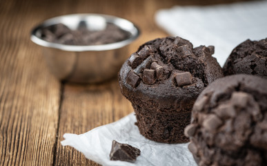 Old wooden table with fresh Chocolate Muffins (close-up shot; selective focus)