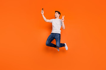 Full length profile photo of funky guy jump high up rejoicing make selfies show v-sign symbol wear...