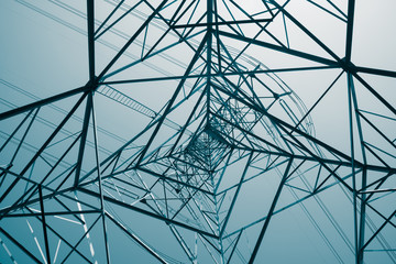 Abstract pattern from bottom view of high voltage pole power transmission tower with clear sky sunny day background in monochrome tone. Green energy, environmental conservation concept.