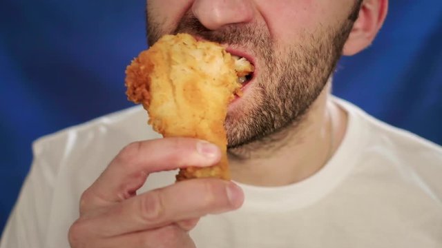 Close-up, a man with stubble eating a chicken leg. Holds nuggets with one hand. It does not lead a healthy lifestyle, impairs health and metabolism. Wrong food. wings and french fries.