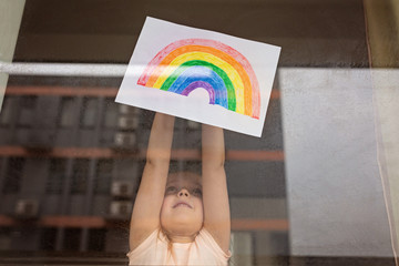 Kid painting rainbow during Covid-19 quarantine at home. Girl near window. Stay at home Social...