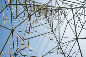 Abstract pattern from bottom view of high voltage pole power transmission tower with clear sky sunny day background. Green energy, environmental conservation concept.