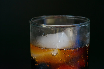 A glass of cola with ice cubes on black background