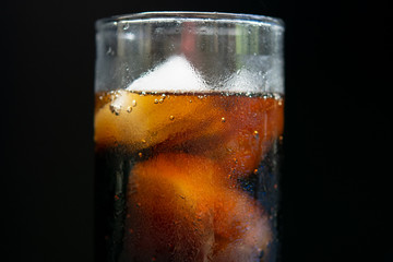 A glass of cola with ice cubes on black background