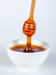 honey dripping from woodin dipper to ceramic bowl
