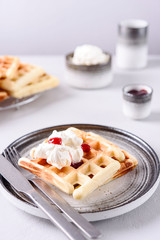 Homemade Belgian Waffles served with whipped cream (Chantilly) and berry jam on grey concrete background. Breakfast. Selective focus