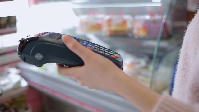A woman applies a Bank card to the payment terminal. Hands close-up. Shop Windows in the background. Concept of purchases with a Bank card