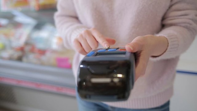The woman enters data into the payment terminal and applies a Bank card to it. Shop Windows in the background. Concept of purchases with a Bank card