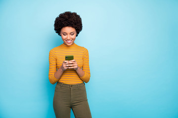 Photo of funny dark skin lady hold telephone hands reading new post comments popular influencer wear yellow striped jumper green pants isolated blue color background