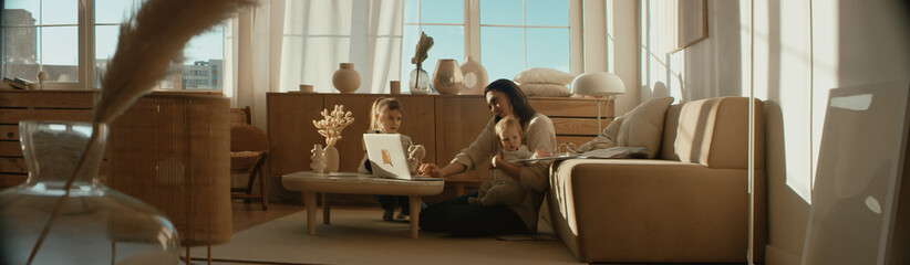 Mother working from home, having a phone call, while her daughters distract her and drawing...