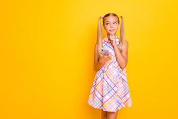 Photo of beautiful little lady hold telephone hand on chin look empty space think new post text ideas for youth blog wear checkered sun dress isolated bright yellow color background