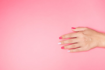 Closeup top view flatlay photography of one beautiful manicured female hand isolated on pastel pink background with empty space in left part of frame.