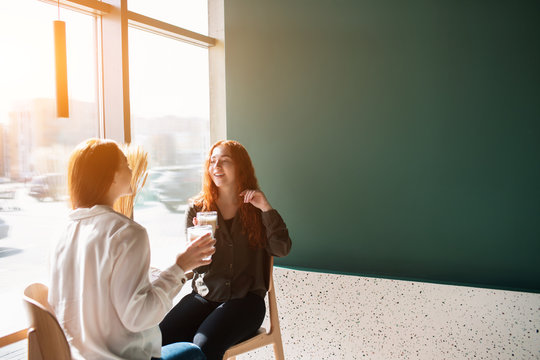 Young women talking in a cafe. Female models drinking coffee and laughing.