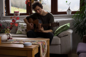 smart home voice activated speaker in home with man on guitar in background. Stay at home.