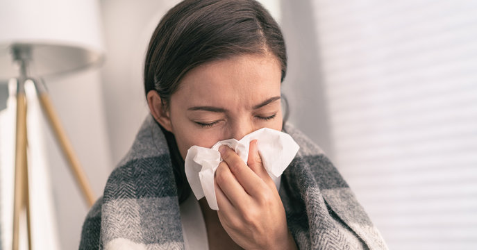 Cough in tissue covering nose and mouth when coughing as COVID-19 hygiene guidelines for coronavirus spread prevention. Asian woman sick with flu at home.