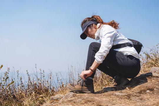 Closeup image of a woman hiker tying shoelaces and getting ready for trekking on the top of mountain