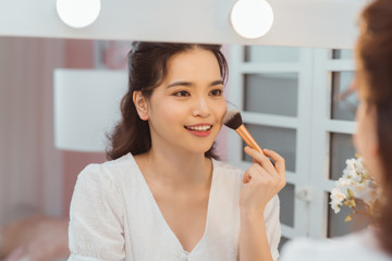 A beautiful young woman sitting at a makeup table and doing her makeup.