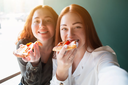 Female models take a selfie on a phone in caffee. Young women smiling and eating pizza