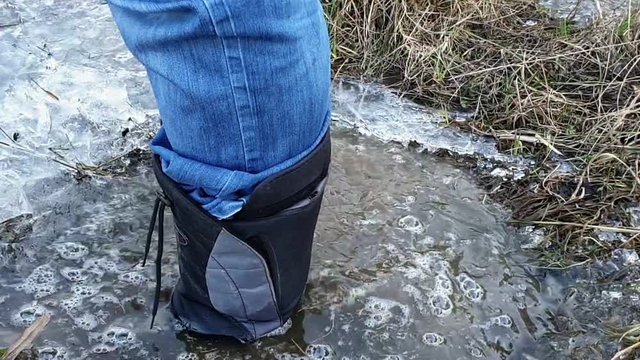 Man's feet in high boots step on ice and fall into puddle