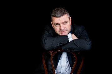 beautiful businessman wearing black suit sitting on black studio background