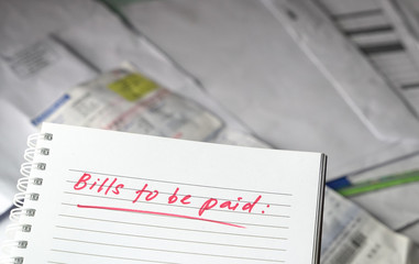 Bills to be paid, red color written words on notebook with bills and invoices at the background