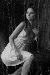 stunning black and white portrait of a sexy young brunette girl in a white midi dress sitting on a high chair on a black background.  Low kay. Beauty and Fashion