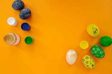 The concept of celebrating Easter. Workplace with cans of paint and colored painted eggs on orange background. Copy space