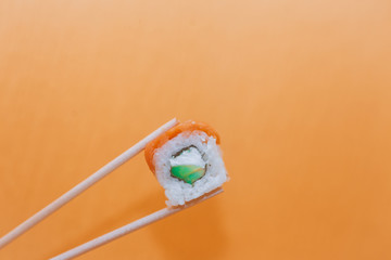 Sushi roll Philadelphia. Sushi and chopsticks. Philadelphia roll with salmon, rice, avocado and sauce on a bright orange background.