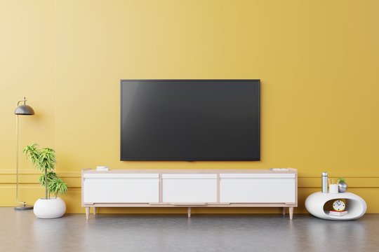 TV on cabinet in modern living room with lamp,table,flower and plant on yellow wall background.