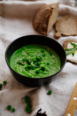 Green peas and spinach puree soup in a black bowl. Vegetarian cream soup on gray background. Healthy eating during quarantine