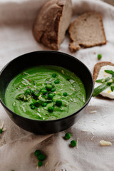 Green peas and spinach puree soup in a black bowl. Vegetarian cream soup on gray background. Healthy eating during quarantine