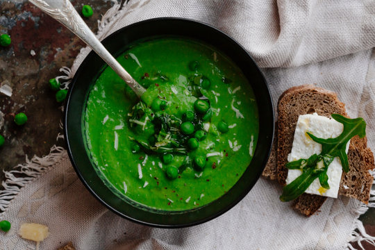 Green Peas And Spinach Puree Soup In A Black Bowl. Vegetarian Cream Soup On Gray Background. Healthy Eating During Quarantine