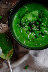 Green peas and spinach puree soup in a black bowl. Vegetarian cream soup on gray background. Healthy eating during quarantine