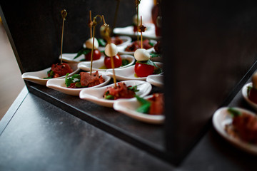 group of appetizer with bacon on a skewer served on a white porcelain spoon close up. catering. selective focus. dark wood background.