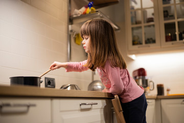 Little caucasian child, 3 years old, cooking on induction kitchen stove in well lit modern kitchen....
