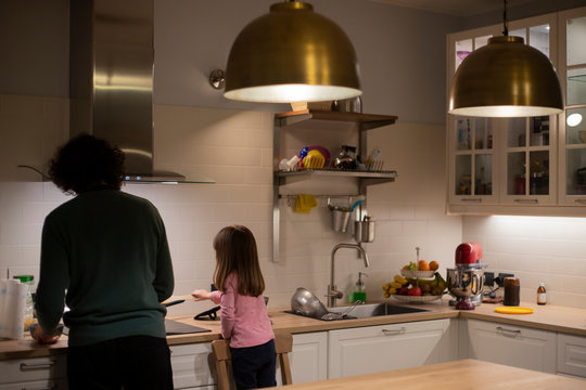 Young father and little child girl, back view, cooking together in modern white kitchen with big brass lamps. Lockdown idea activity for preschoolers.