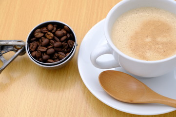 Coffee cup and beans on wooden kitchen table. Top view with morning sunlight